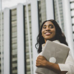 businesswoman holding laptop standing foreground of business cen